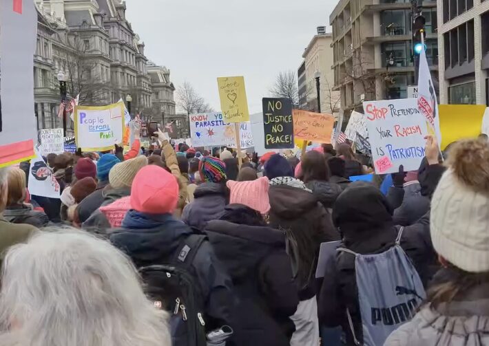 A mass of people marching in a protest wile holding sign.