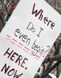 Protest sign displaying: Where do I even begin. Here. Now.